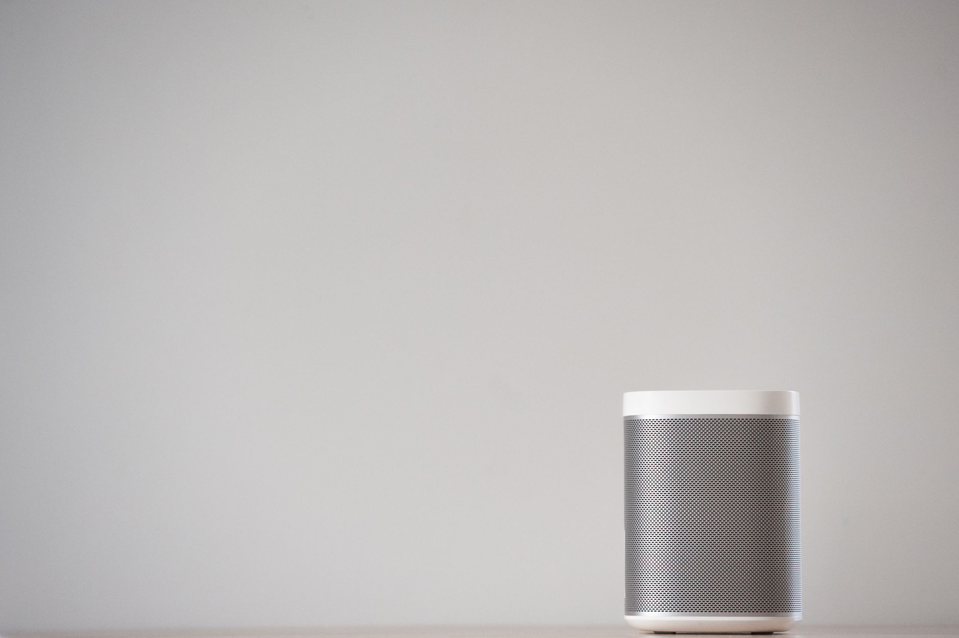cách treo loa lên tường đúng kỹ thuật - A sleek, wireless smart speaker on a wooden table against a plain wall.