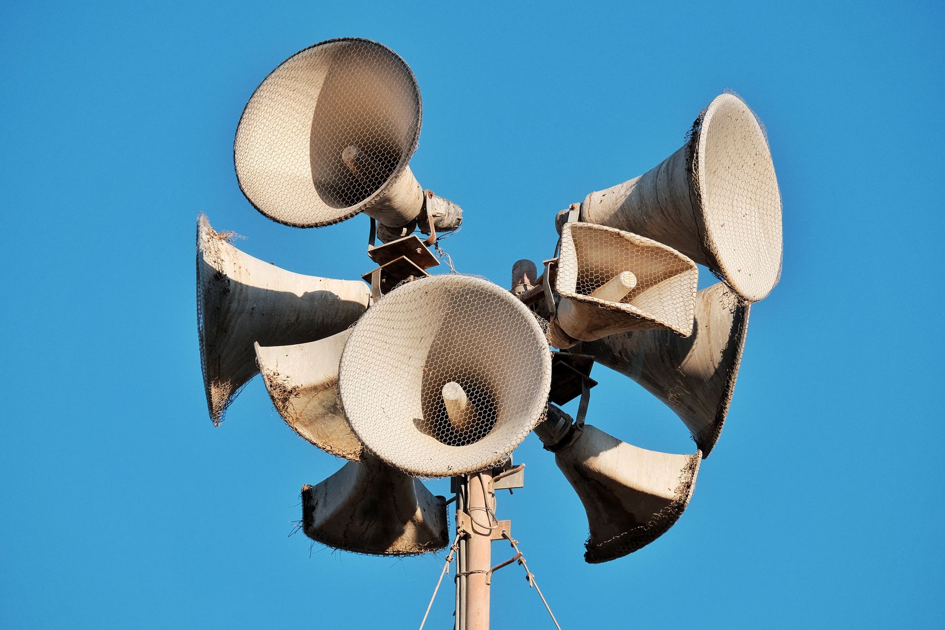 Hướng Dẫn Phối Ghép Amply Với Loa Đúng Trở Kháng - Close-up of multiple aged megaphones on a pole against a clear blue sky.
