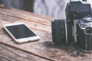 Âm thanh Analog vs Digital khác nhau thế nào - A vintage camera alongside a smartphone on a rustic wooden table surface.