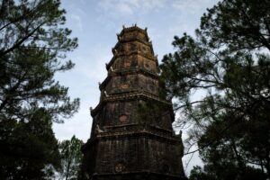 Âm thanh nhà thờ, chùa - A historic pagoda tower rises elegantly amidst pine trees in Hue, Vietnam, showcasing ancient architecture.
