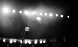 Amply Karaoke Loại Nào Tốt? Top Dòng Đáng Mua - A dramatic black and white photo of a microphone onstage with bright concert lights.