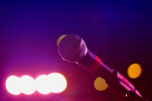 Amply Và Cục Đẩy Khác Nhau Như Thế Nào? Nên Chọn Loại Nào? - Colorful stage lighting highlights a microphone in a close-up view, perfect for music and performance themes.