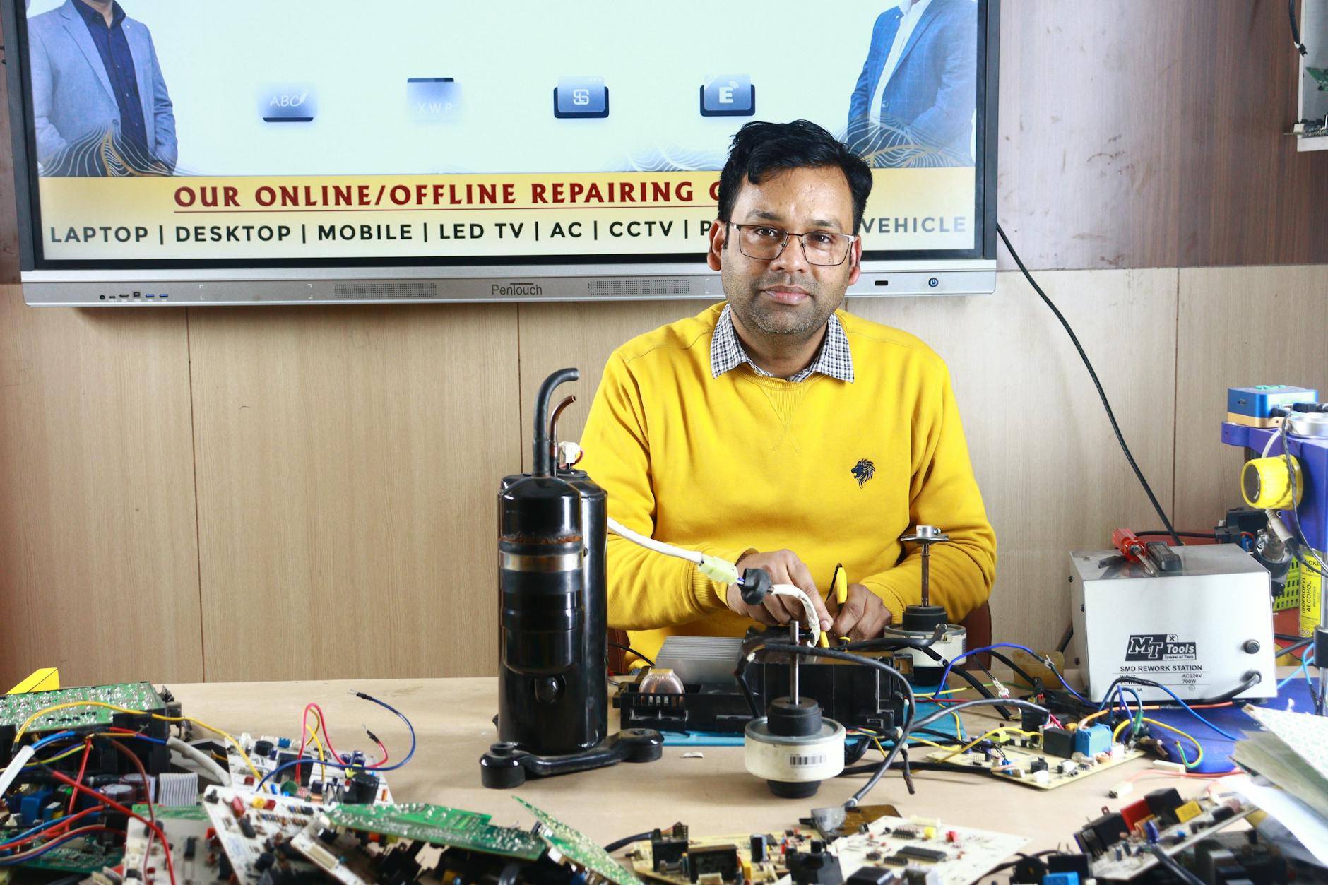 Ổn áp/lọc nguồn cho dàn âm thanh có cần không - Man engages in air conditioner repair at New Delhi training center, surrounded by electronic components.