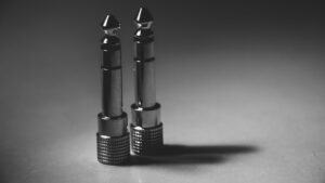 Cách chọn jack, đầu nối âm thanh - Black and white close-up of metallic audio jack connectors on a flat surface, showcasing modern technology.