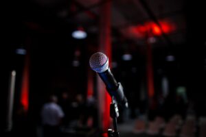 Cách Chọn Loa Karaoke Hay Theo Diện Tích Phòng - Dynamic photo of a microphone on stage with red backlighting, ideal for live performance themes.