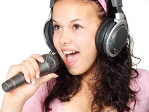 Cách Chống Hú Cho Loa Karaoke Triệt Để - A young woman passionately singing with headphones and microphone on a white background.