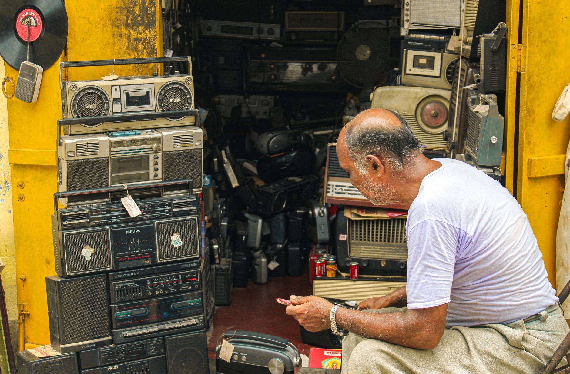 Cách lắp đặt dàn karaoke gia đình hoàn chỉnh - Man inspecting vintage electronics and retro radios in cluttered shop full of antique audio equipment.