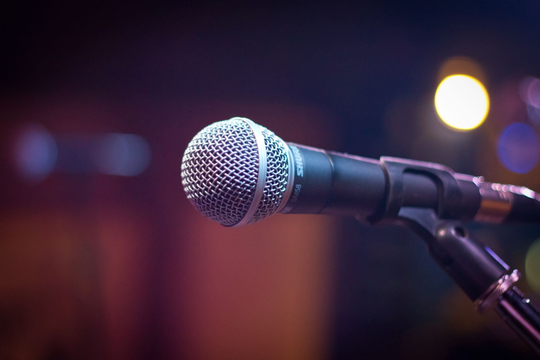 Amply Karaoke Loại Nào Tốt? Top Dòng Đáng Mua - Dynamic microphone on stand with blurred stage lights in background.