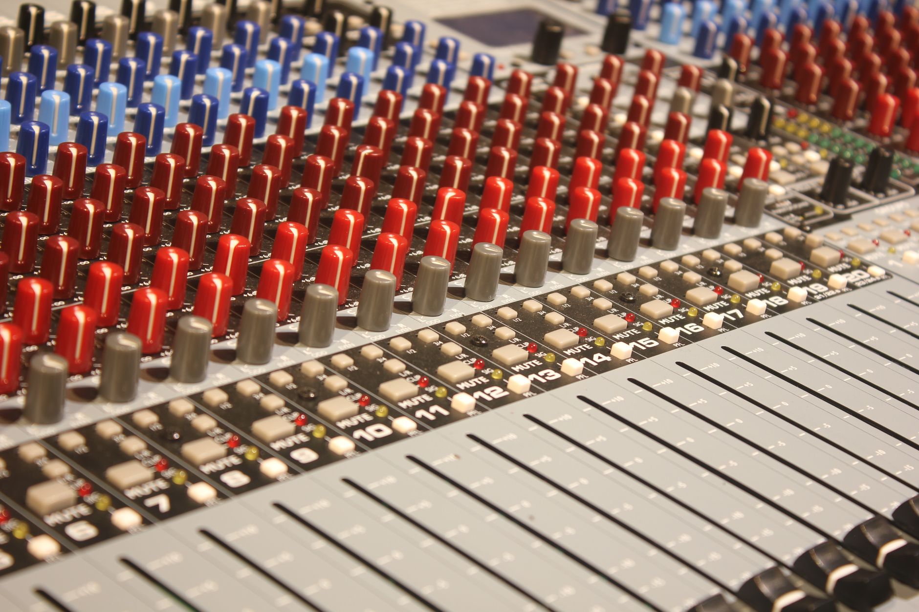 thay biến áp amply - Close-up of audio mixing console with red and blue knobs, ideal for music production.
