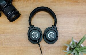 Dây tín hiệu (canon/XLR, jack 6 ly) khác nhau thế nào - Top view of black headphones, camera, and potted plant on a wooden table, representing modern technology essentials.