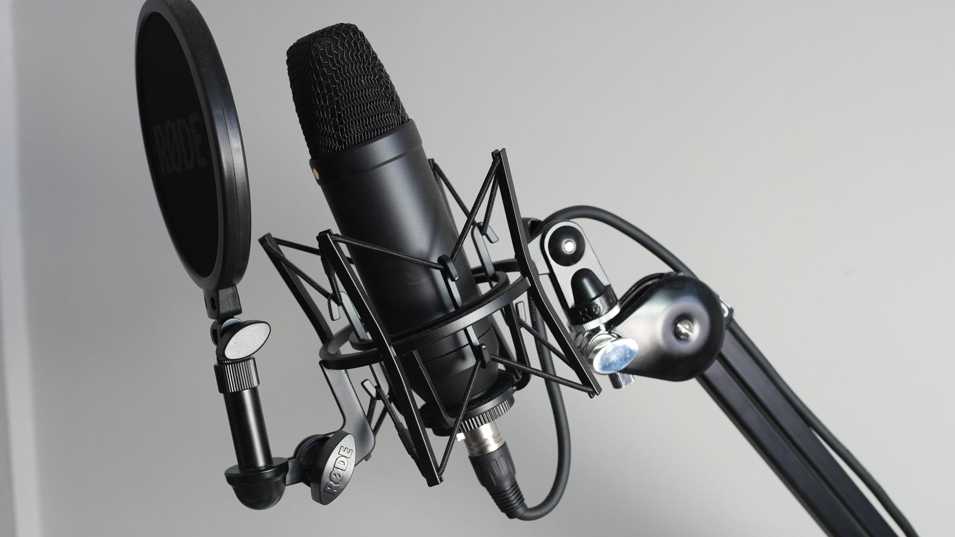 Micro Có Dây Bị Đứt Tiếng, Chập Chờn - Close-up of a black condenser microphone with shock mount and pop filter for high-quality studio recordings.