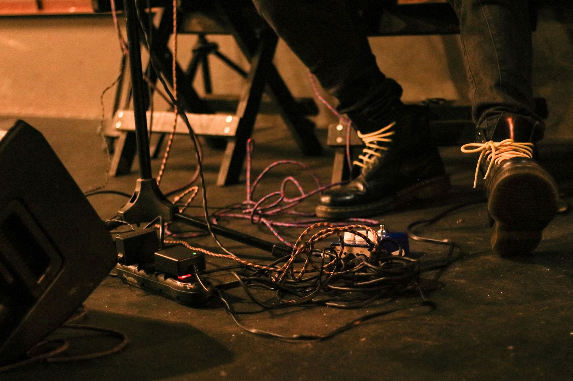 Các loại dây loa, cách chọn tiết diện dây - Close-up of a musician's feet on stage surrounded by cables and audio equipment.