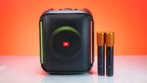 Hướng Dẫn Đấu Nối Dàn Karaoke Chuẩn Cho Người Mới - A wireless speaker with two microphones, set against a vivid orange background for a studio shoot.