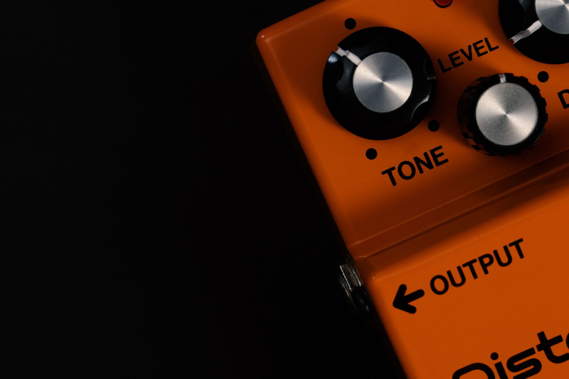 Cách Sử Dụng Amply Đúng Cách Để Bền & Hay - Detailed close-up of an orange guitar distortion pedal showcasing tone and level knobs.