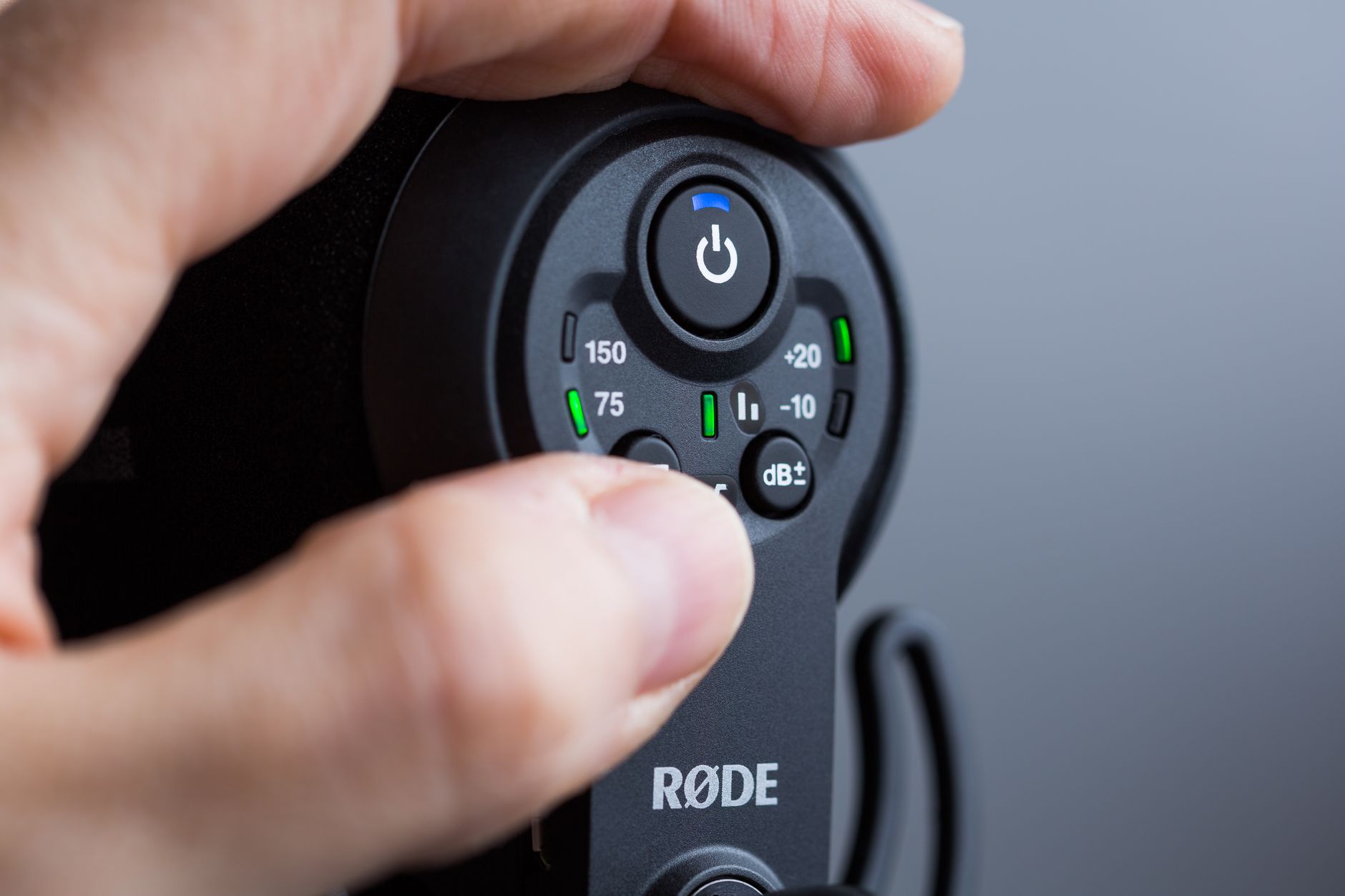 Sửa Micro Không Dây Bị Rè, Mất Sóng - Detailed close-up of a hand adjusting a Røde microphone's controls, showcasing precision technology.