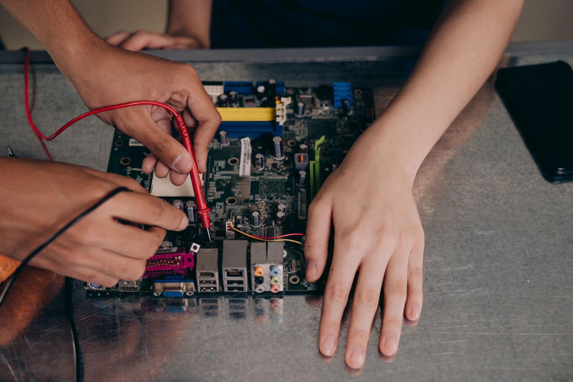 Cách Chống Hú Cho Loa Karaoke Triệt Để - Hands working with electrical tester on motherboard, showcasing technical repair skills.