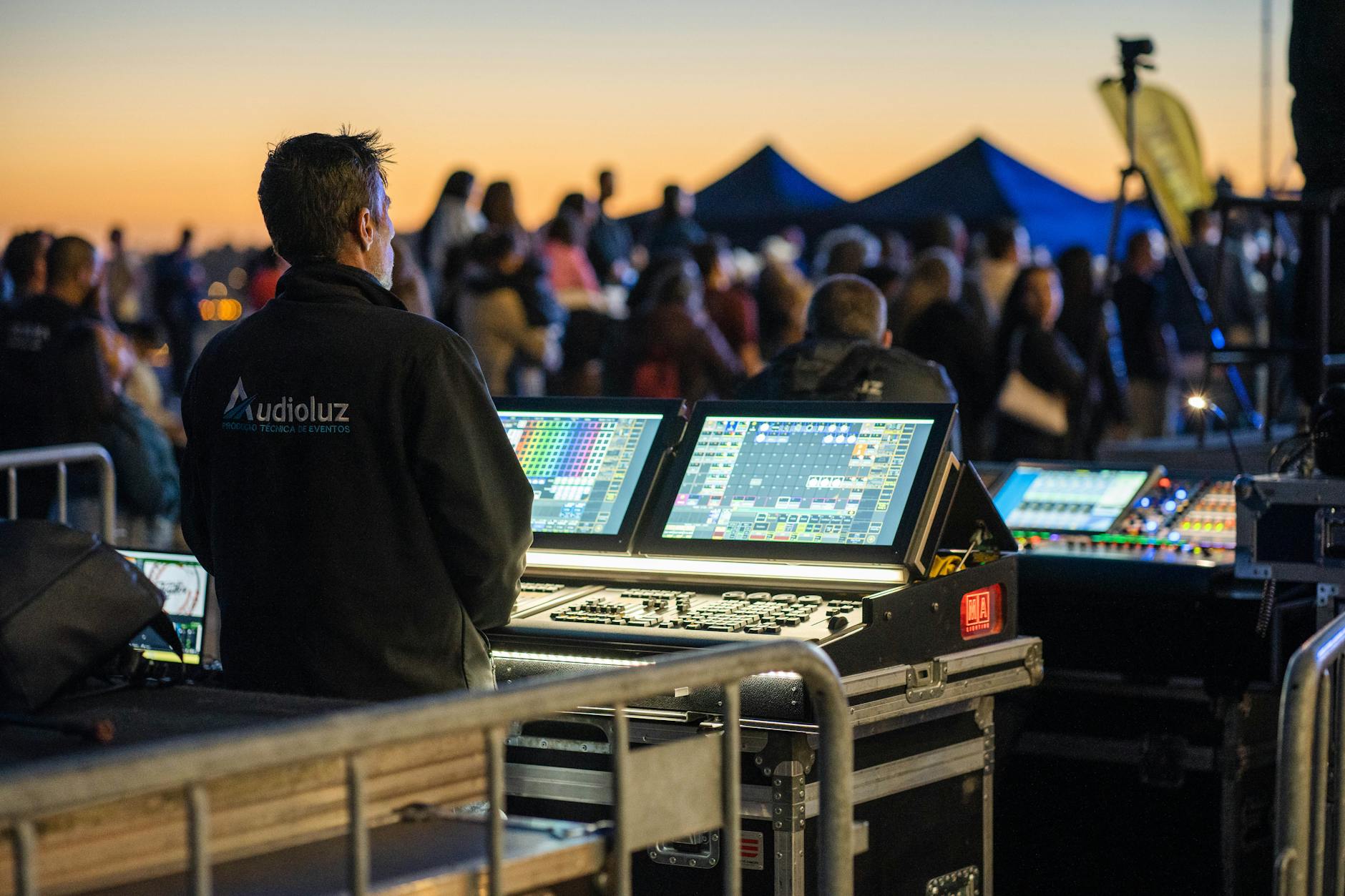 Âm thanh sân khấu ngoài trời cần gì - Technician managing sound and lighting panels during an outdoor event at sunset.