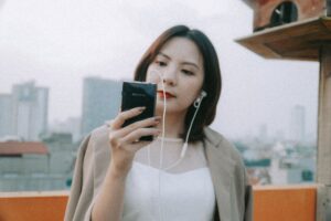 Micro Có Dây Bị Đứt Tiếng, Chập Chờn - Woman in a white dress enjoying music with earbuds on a rooftop with a city skyline background.