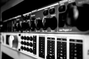 Sửa Vang Số Bị Treo, Đơ Nút - Detailed black and white close-up of an audio mixer highlighting various control knobs and switches.
