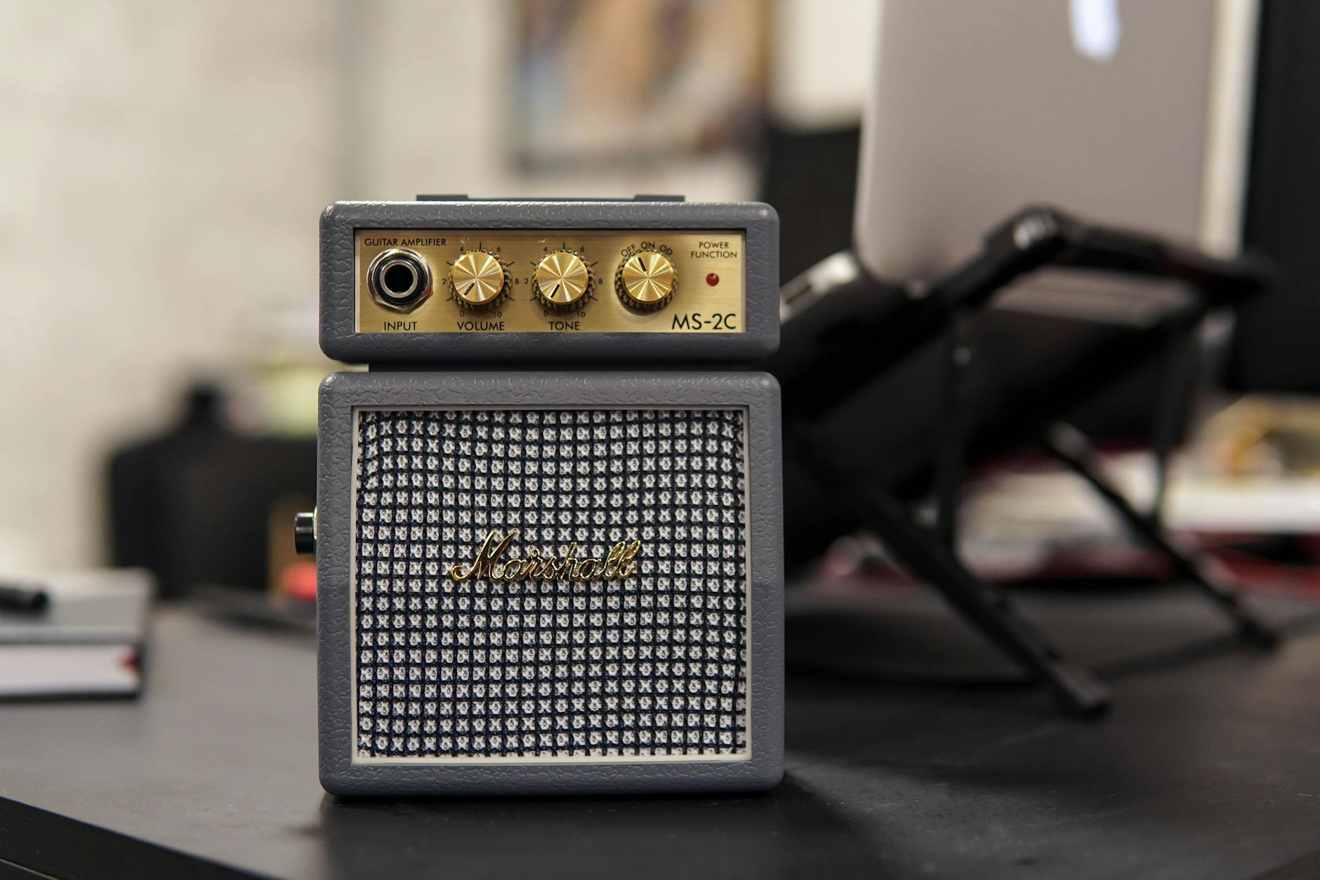 Amply Và Cục Đẩy Khác Nhau Như Thế Nào? Nên Chọn Loại Nào? - Marshall MS-2C mini guitar amplifier on a desk with blurred office background.