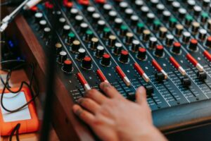 Amply hỏng chiết áp - Close-up of a hand adjusting controls on a professional sound mixer in a recording studio.
